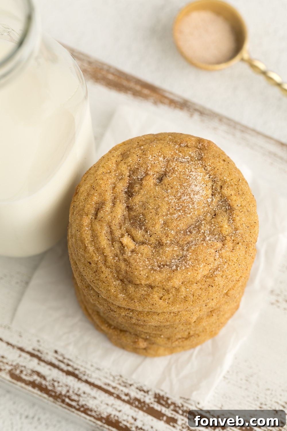 Spiced Pumpkin Snickerdoodle Cookies 17 Pumpkin Snickerdoodle Cookies stacked on top of one another by a glass of milk and a small spoon of cinnamon sugar sitting behind it on table