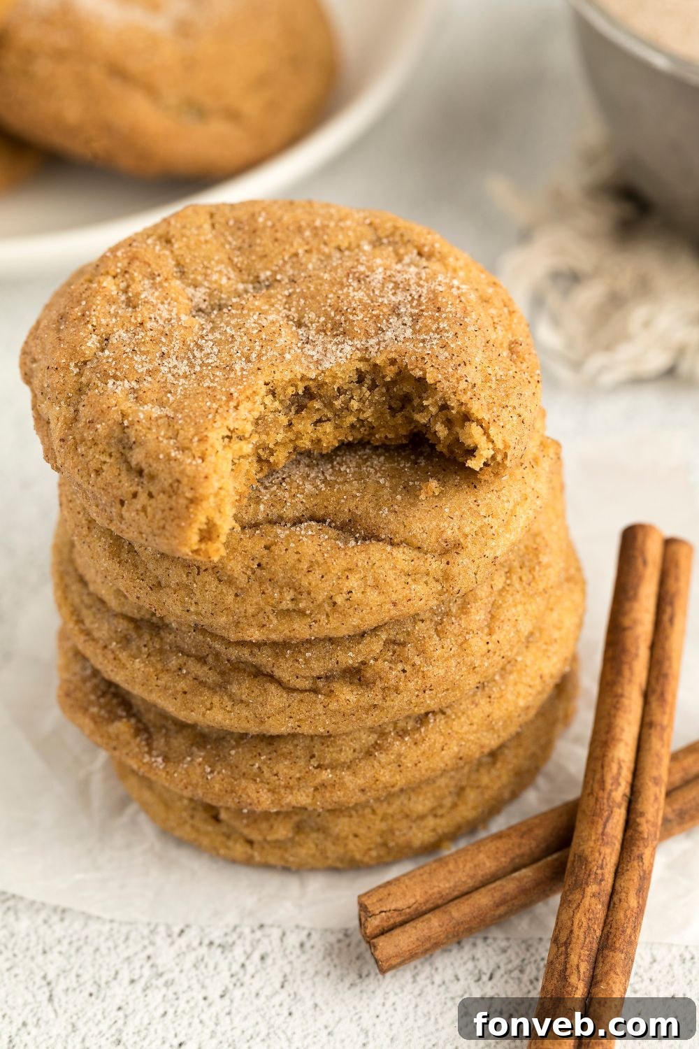 Spiced Pumpkin Snickerdoodle Cookies 18 Pumpkin Snickerdoodle Cookies stacked on table with the top one with a bite taken out of it, and cinnamon sticks in front of cookies