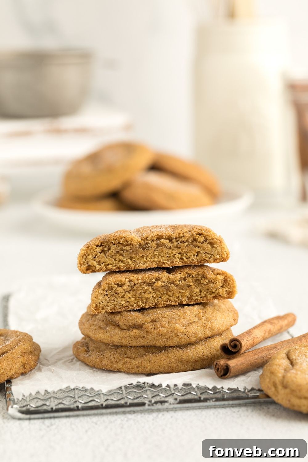 Spiced Pumpkin Snickerdoodle Cookies 19 Pumpkin Snickerdoodle Cookies cut in half and placed on top of one another showing the centers of the cookies with a plate and milk behind it farther back on table