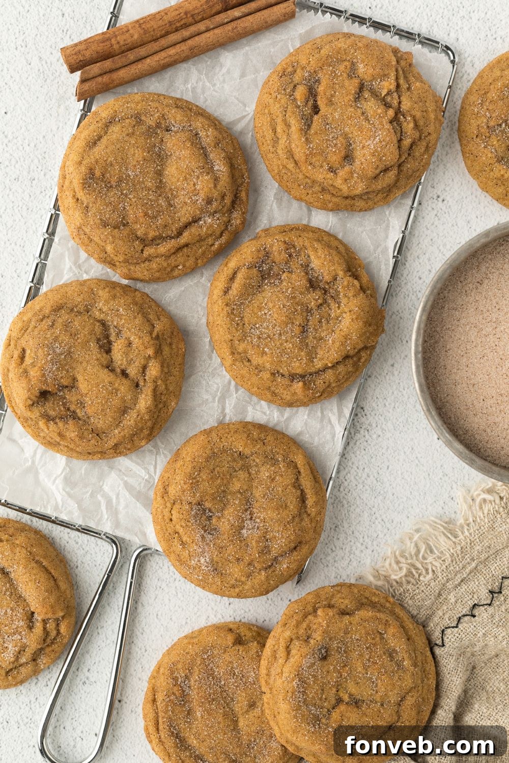 Spiced Pumpkin Snickerdoodle Cookies 21 Pumpkin Snickerdoodle Cookies spread out on a white table with cinnamon sugar to side and cinnamon sticks around cookies