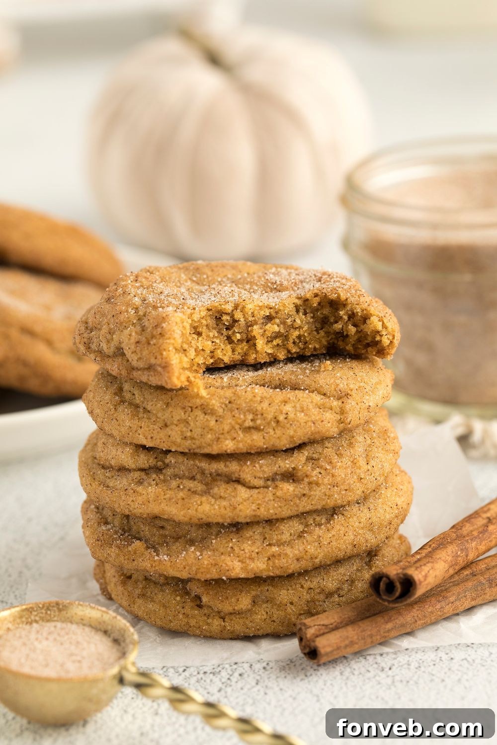 Spiced Pumpkin Snickerdoodle Cookies 23 Pumpkin Snickerdoodle Cookies on a plate stacked with the top one with a bite taken out of it and cinnamon sticks to the side of plate