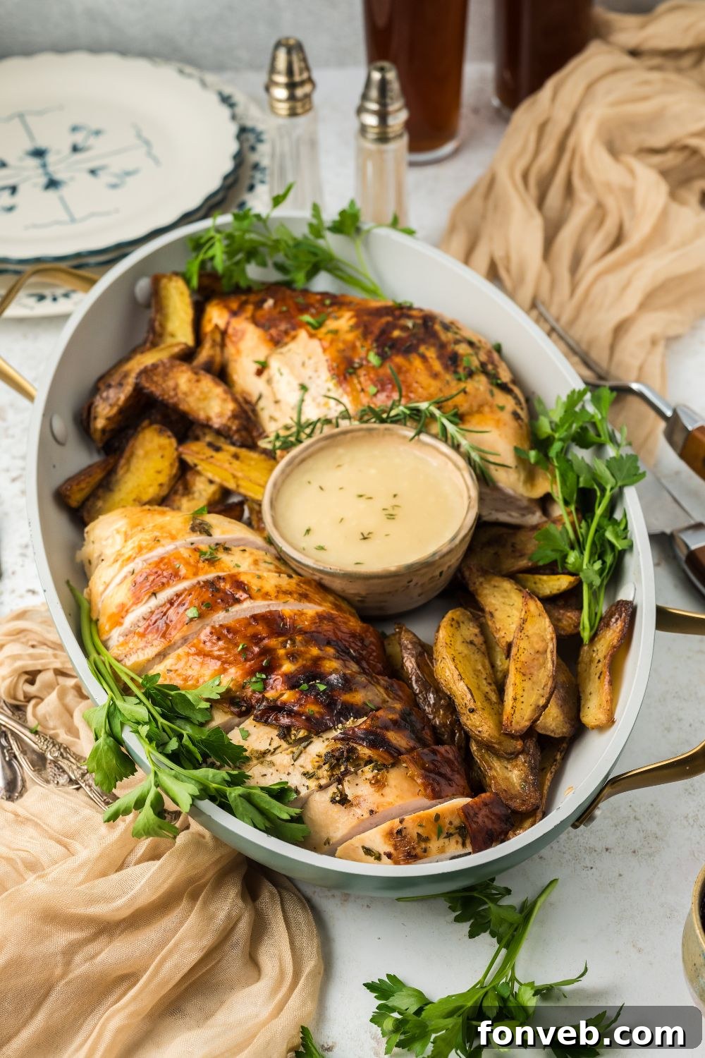 Roasted Turkey Breast in a platter on white table full of potatoes, greens, and a small bowl of gravy in center of the platter