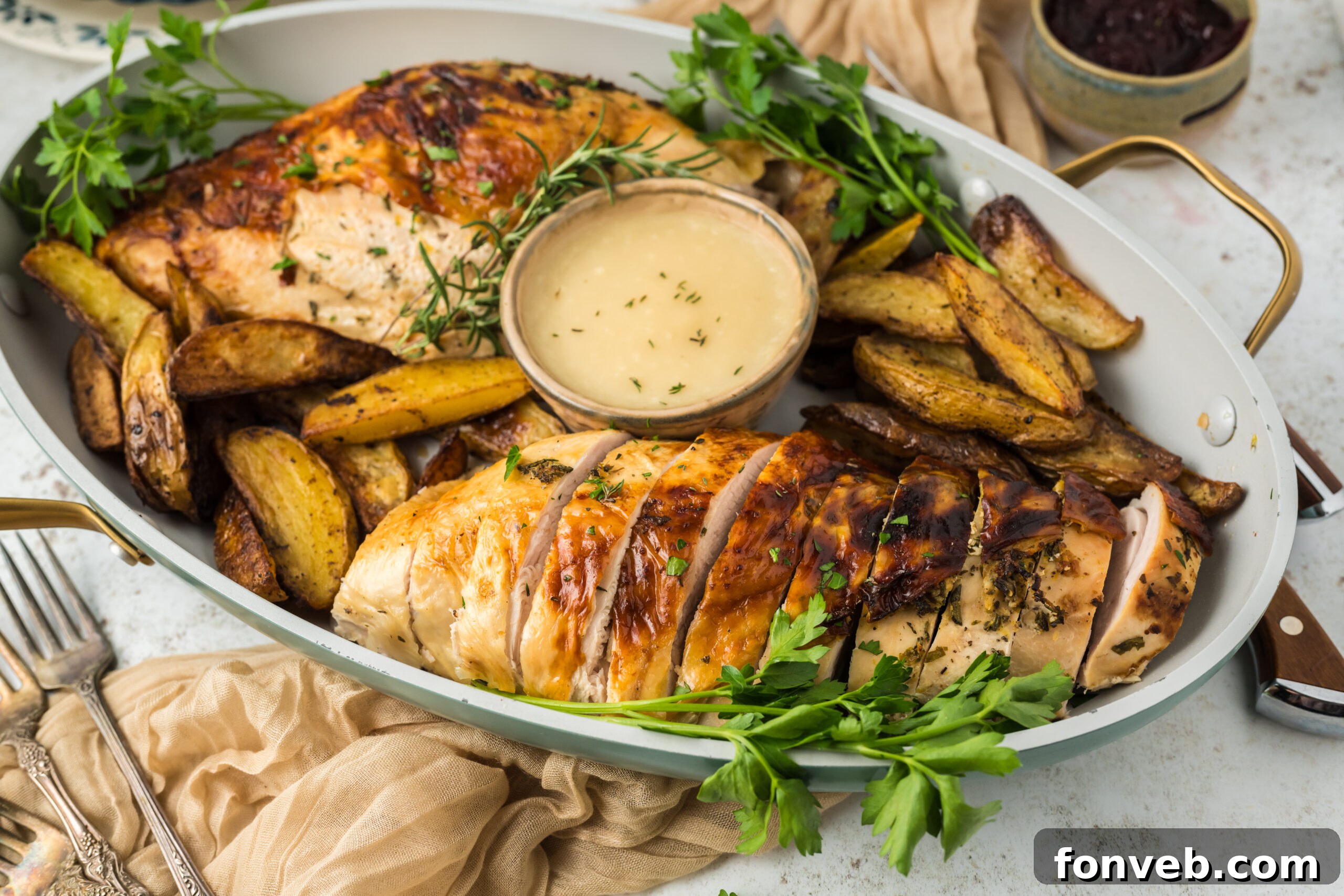 Large platter on white table with sliced roasted turkey on it, with a bowl of sauce and roasted potatoes
