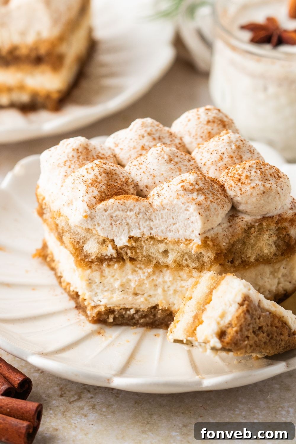 Eggnog Tiramisu on a plate with a bite on the fork with a plate with another slice of eggnog dessert