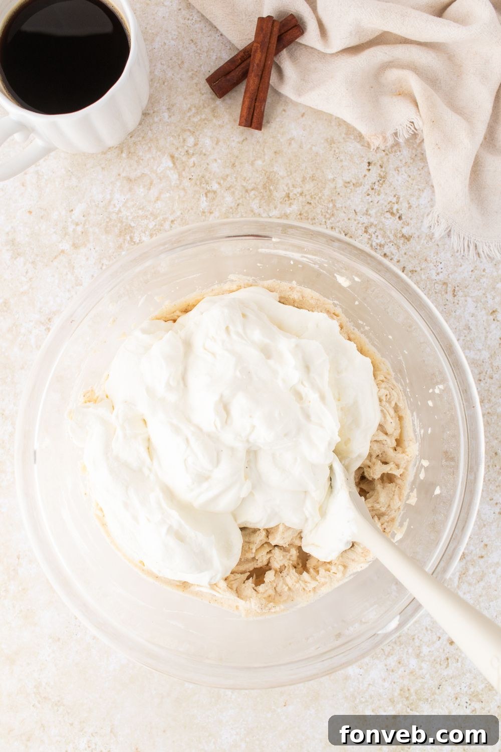 a glass bowl on table folding in whipped cream into the eggnog tiramisu
