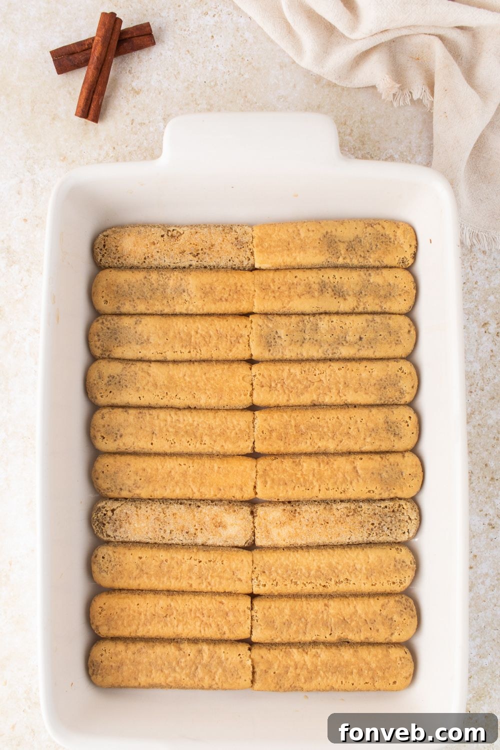 a single layer of dipped ladyfinger cookies in a white casserole pan 
