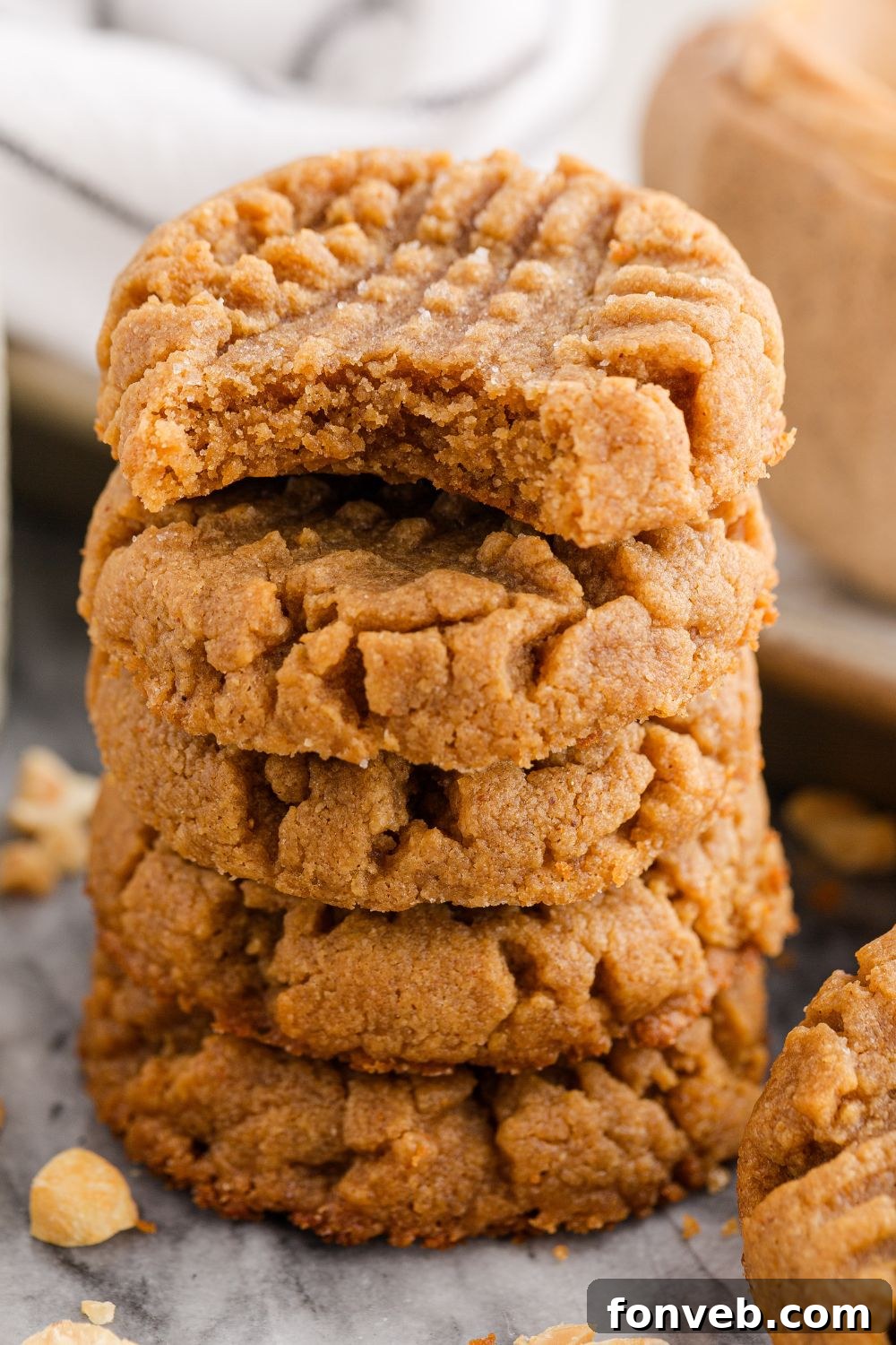 Easy 4-Ingredient Flourless Peanut Butter Cookies 11 stack of peanut butter cookies on table with a bite taken out of the cookie with peanuts scattered around the table