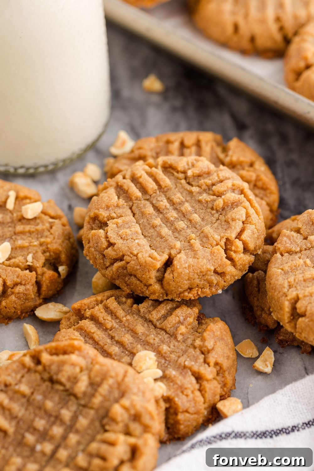 Easy 4-Ingredient Flourless Peanut Butter Cookies 16 4 Ingredient Peanut Butter Cookies spread around table with a tray full of cookies behind and a tall jar of milk