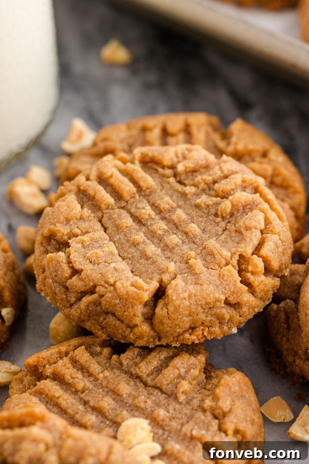 Easy 4-Ingredient Flourless Peanut Butter Cookies 21 marble counter with a tall glass of milk and nuts around the cookies stacked on the table