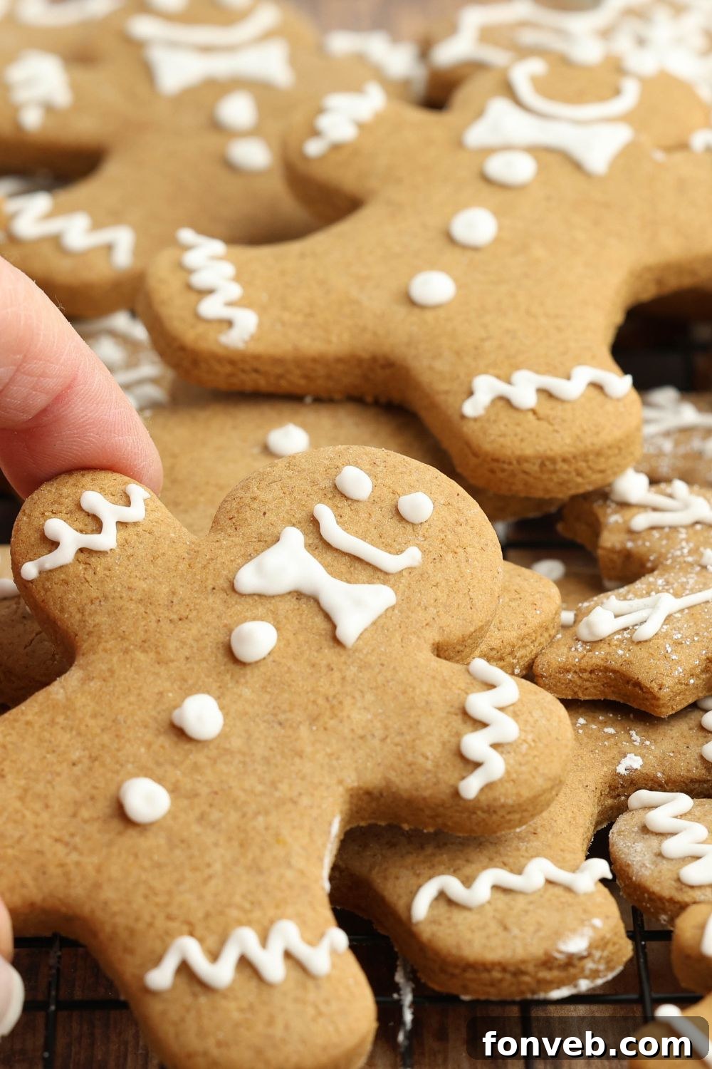 Dazzling Christmas Gingerbread Adorned With Royal Icing 13 hand grabbing one of the cookies scattered on the table