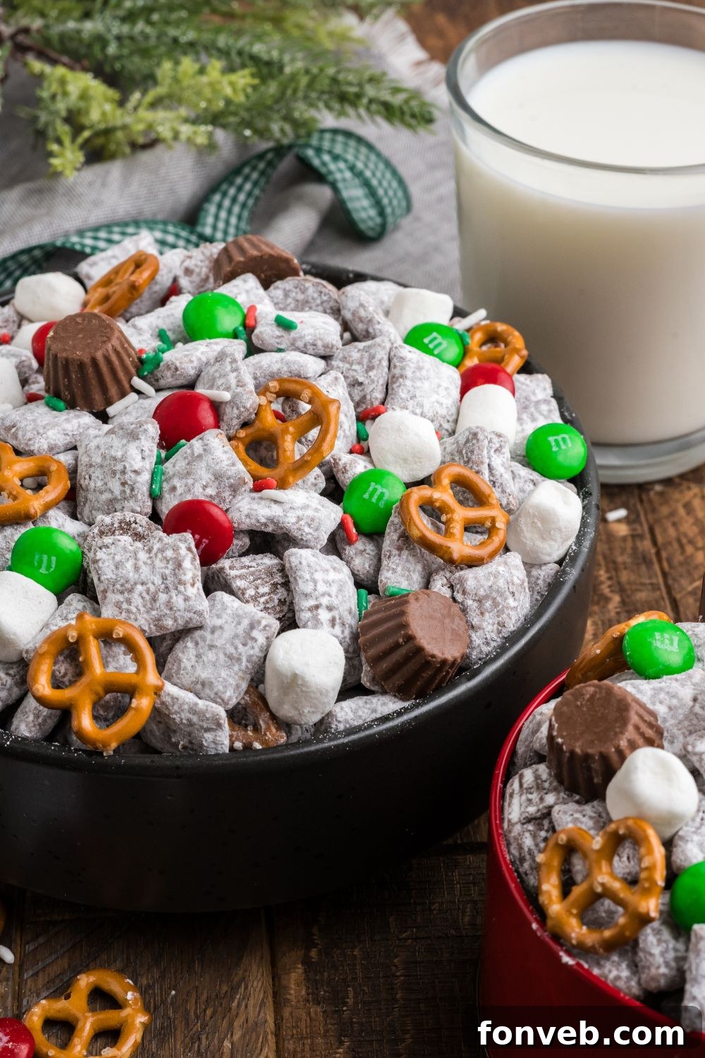Christmas Chex Mix in a black bowl on table with a glass of milk to side 