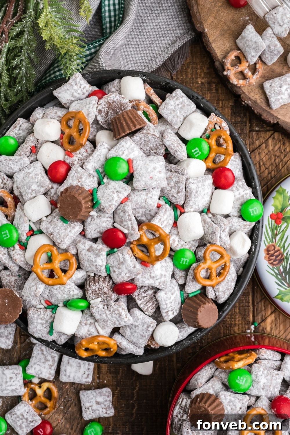 Christmas Chex Mix in a large bowl on table overflowing on wooden table with smaller bowls around table with more 