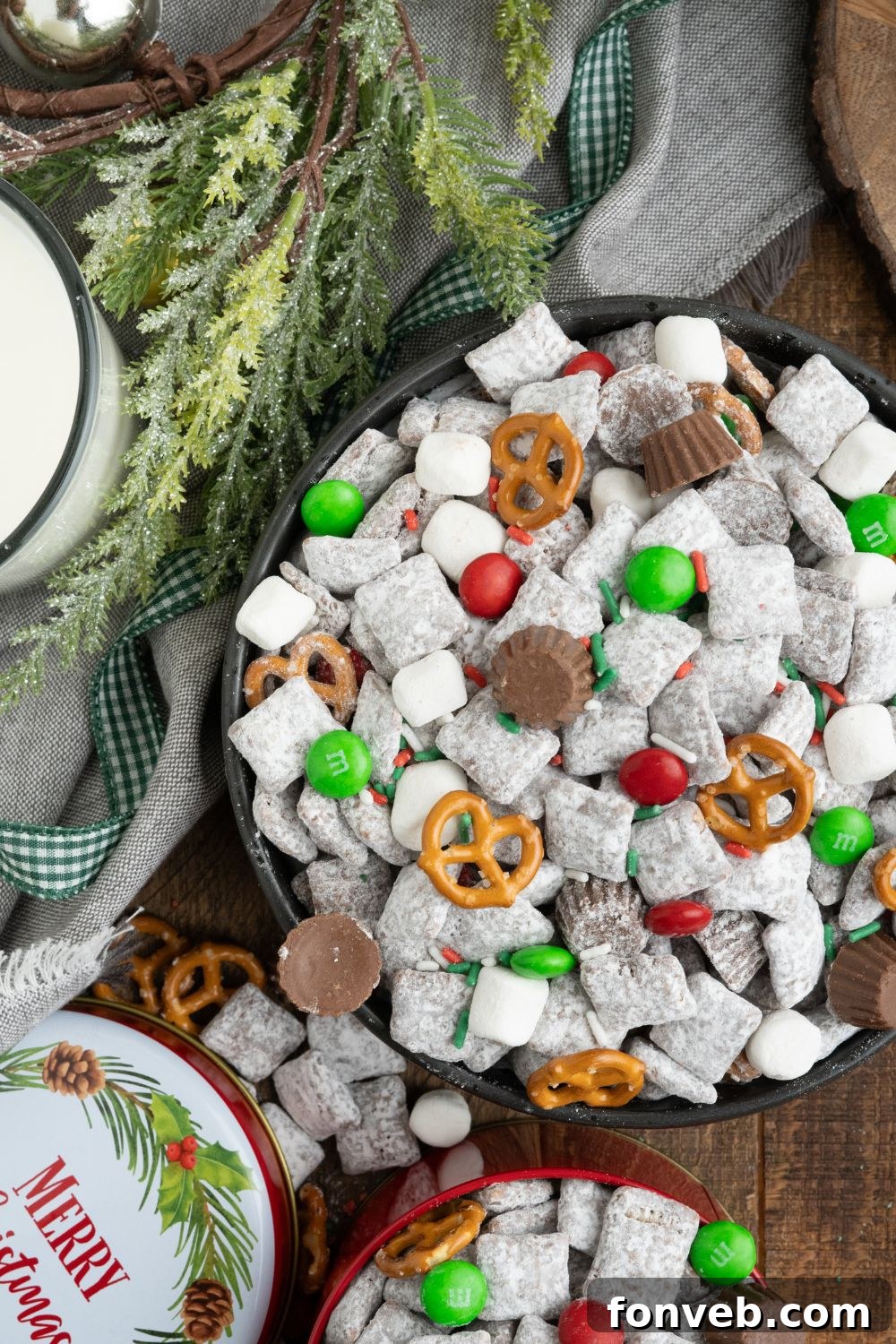 Christmas Chex Mix scattered around the table with a christmas decor to side and a glass of milk 