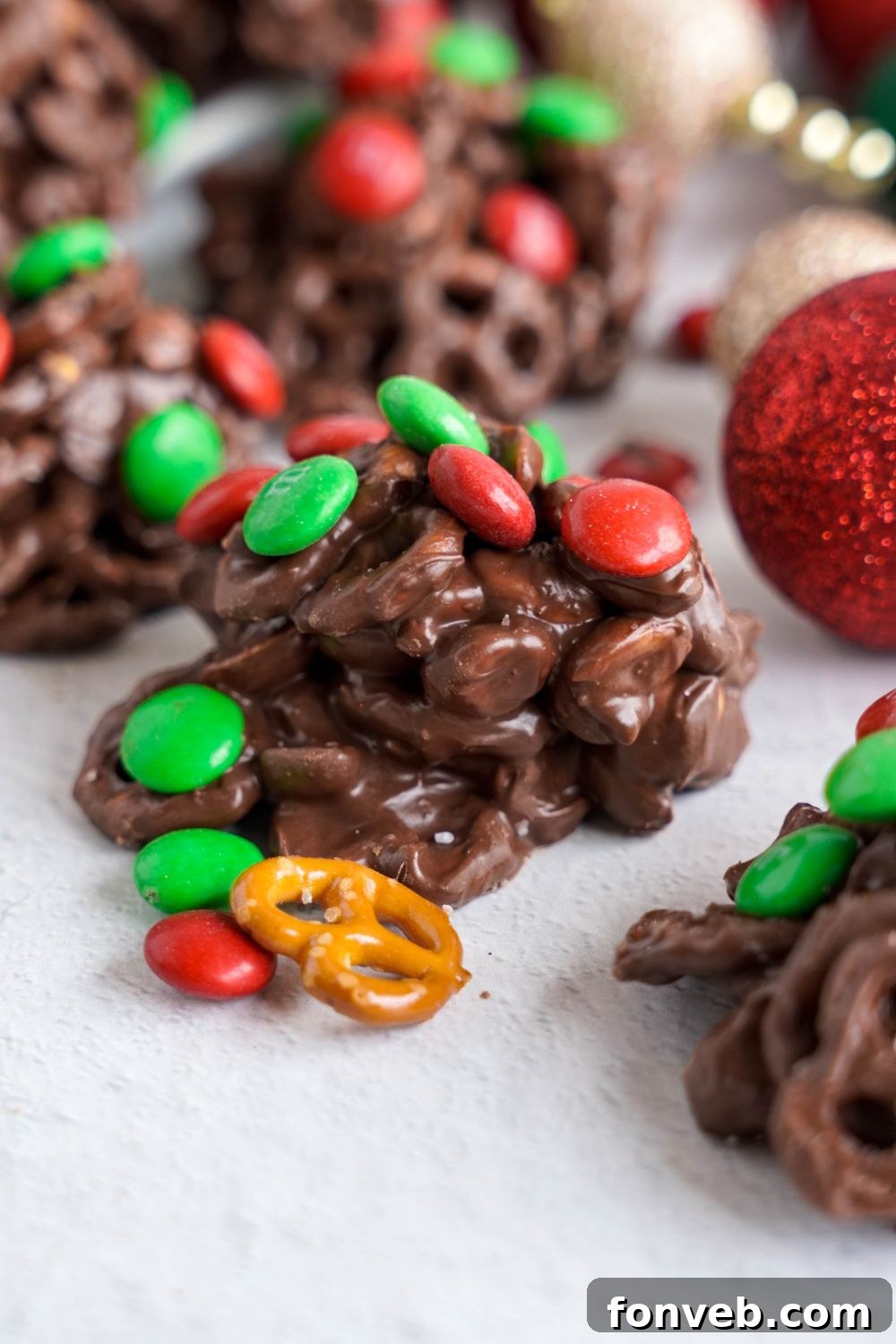 Sweet and Salty Slow Cooker Holiday Clusters 2 Crockpot Chocolate Pretzel Christmas Candy placed around a white table with a christmas ornament to side