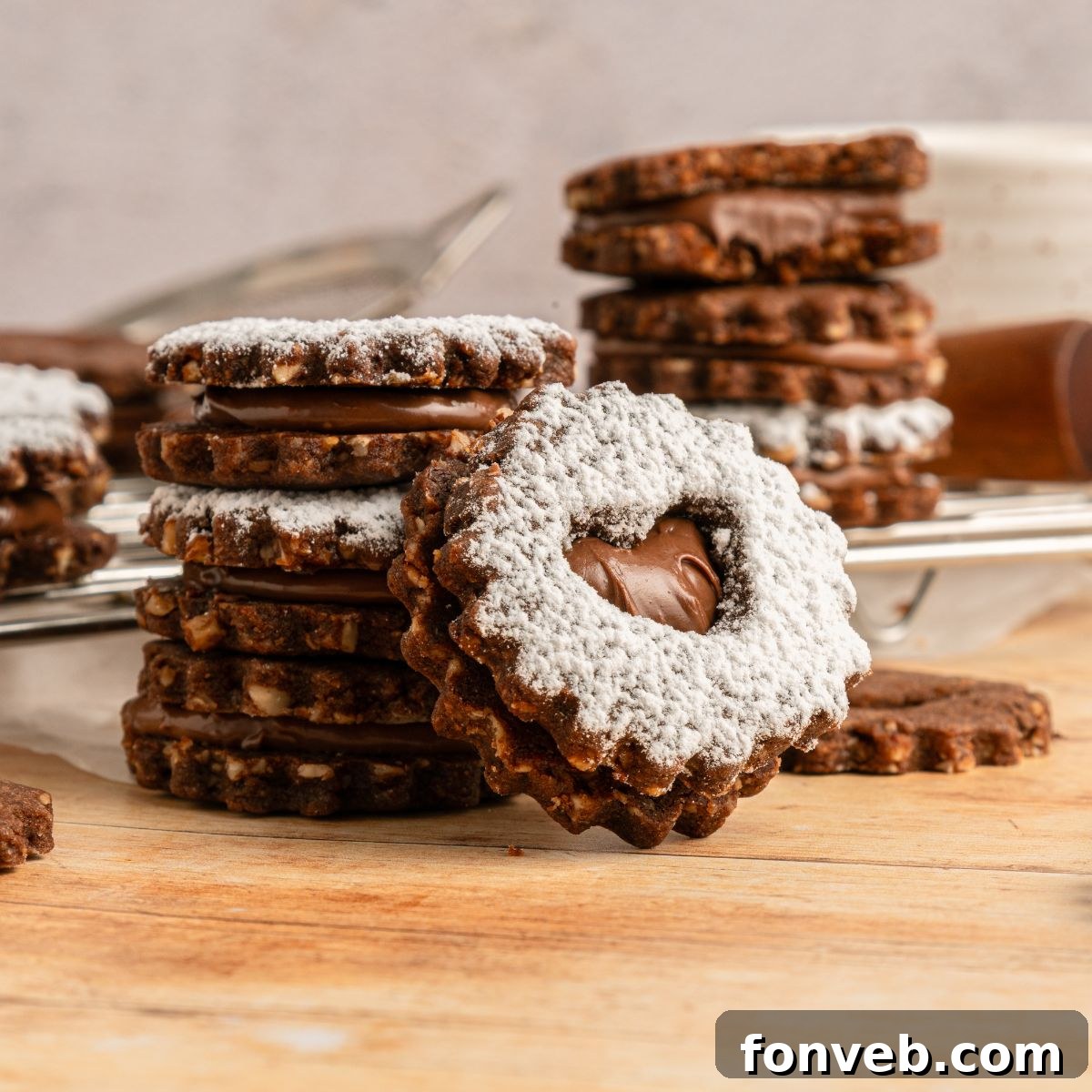 Chocolate Linzer Cookies stacked on the table in piles with one that has a bite taken out of it 