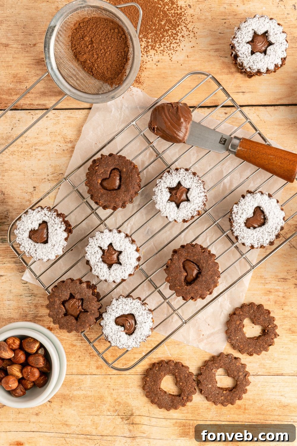 Chocolate Linzer Cookies on a table with a cooling rack with some cookies assembled and others just placed around the table 