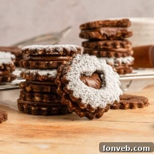 Chocolate Linzer Cookies stacked on the table in piles with one that has a bite taken out of it