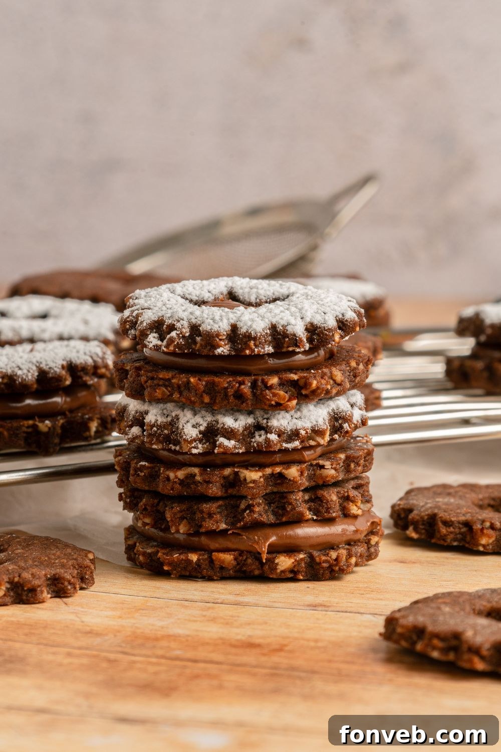 Chocolate Linzer Cookies stacked on table with more cookies around the wooden table 