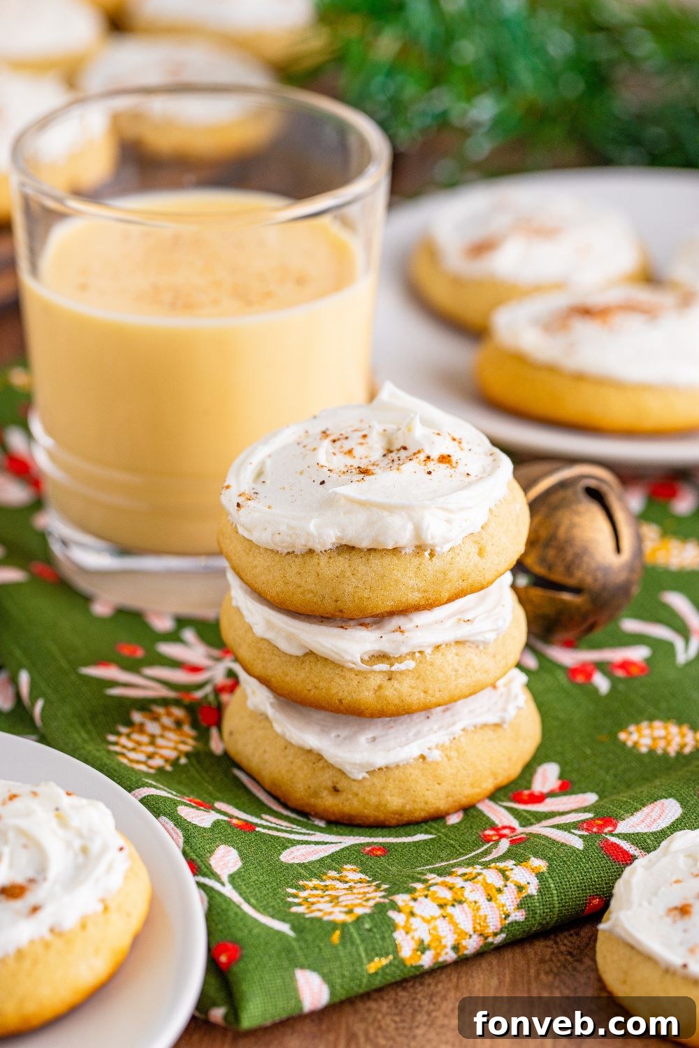 Soft Frosted Eggnog Cookies stacked on a table with more plates of cookies around and a glass full of eggnog