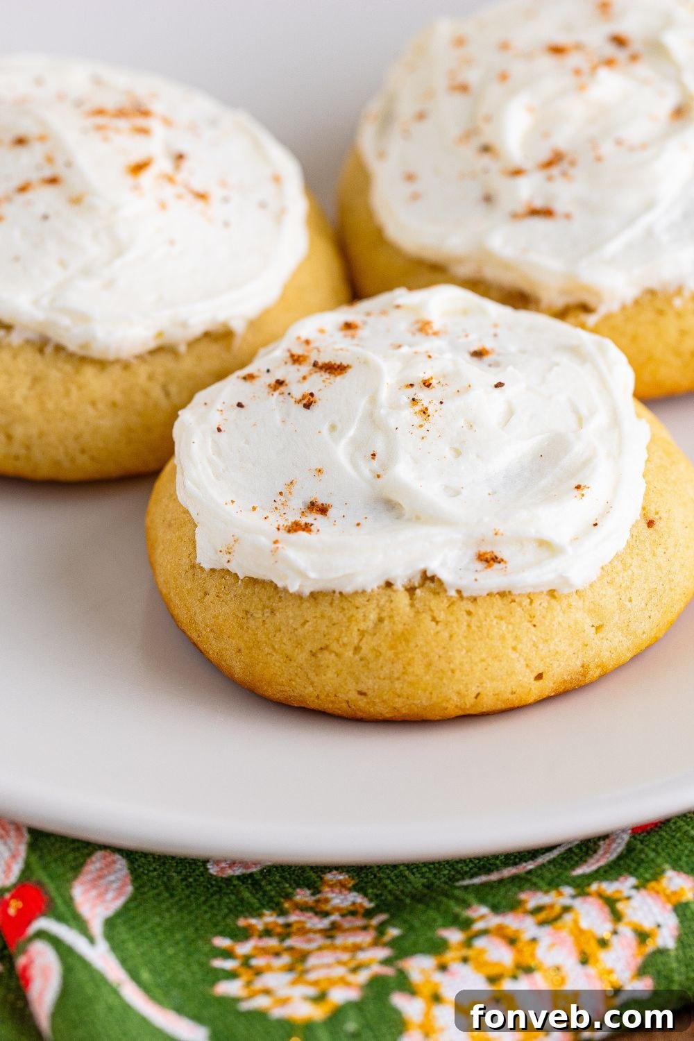 white plate with three Soft Frosted Eggnog Cookies placed on it and a green holiday napkin under the plate