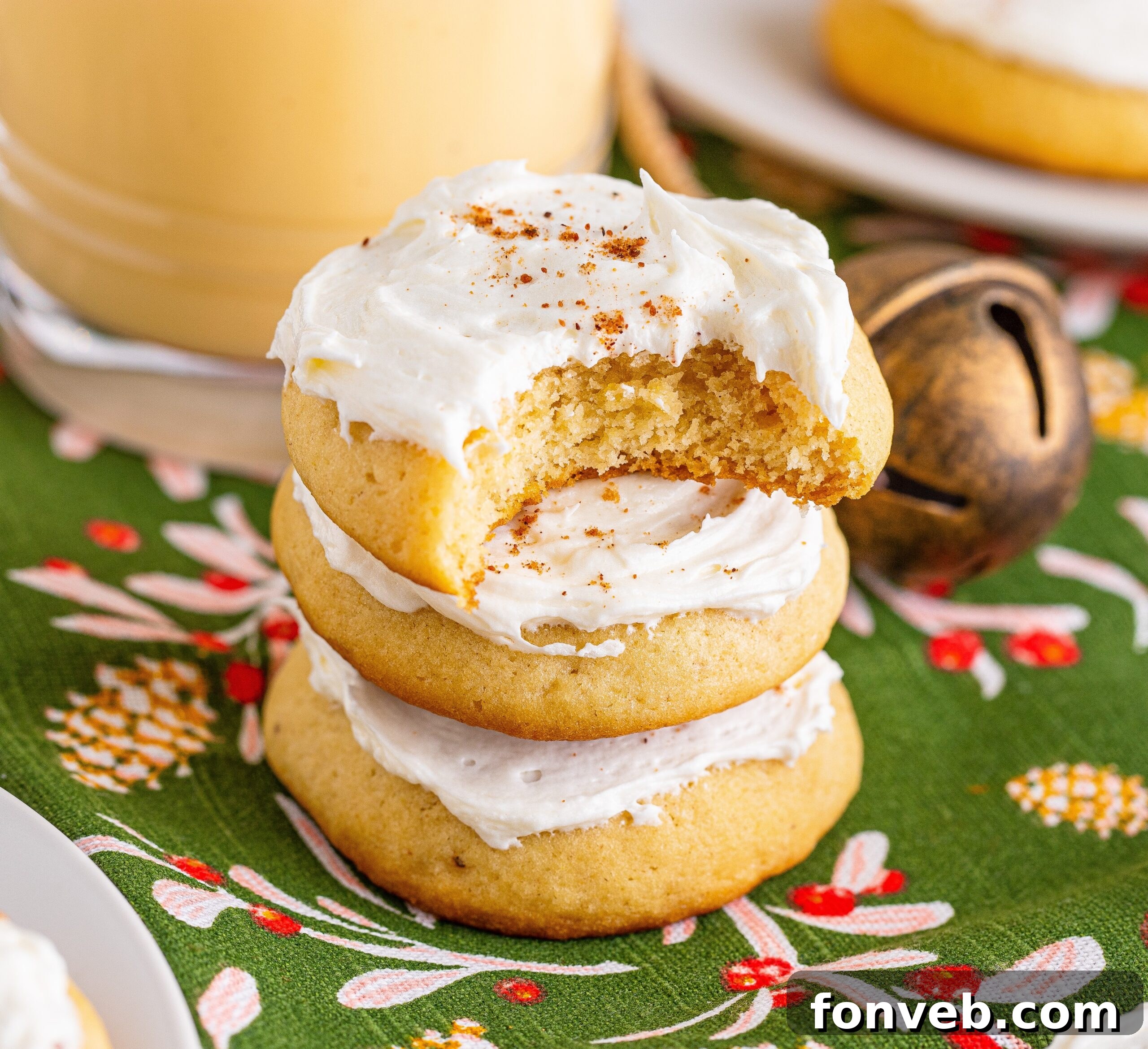 Soft Frosted Eggnog Cookies stacked on a table with a bite missing from the top cookie