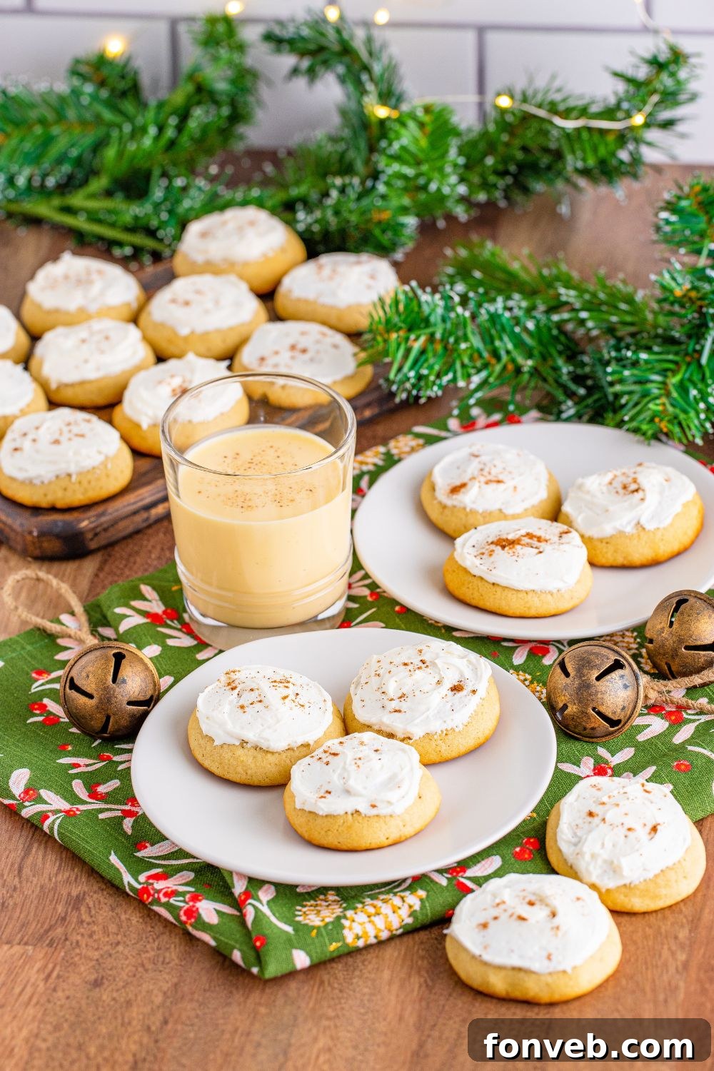 wooden table full of Soft Frosted Eggnog Cookies on a tray and white plates and then a glass of eggnog