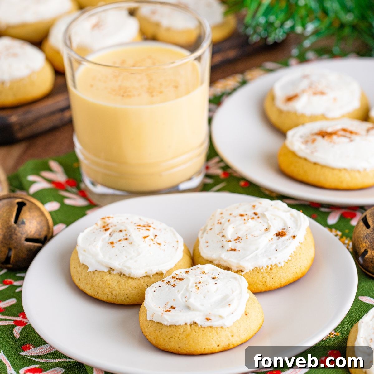 Soft Frosted Eggnog Cookies on plates on a table with a glass of eggnog to the side