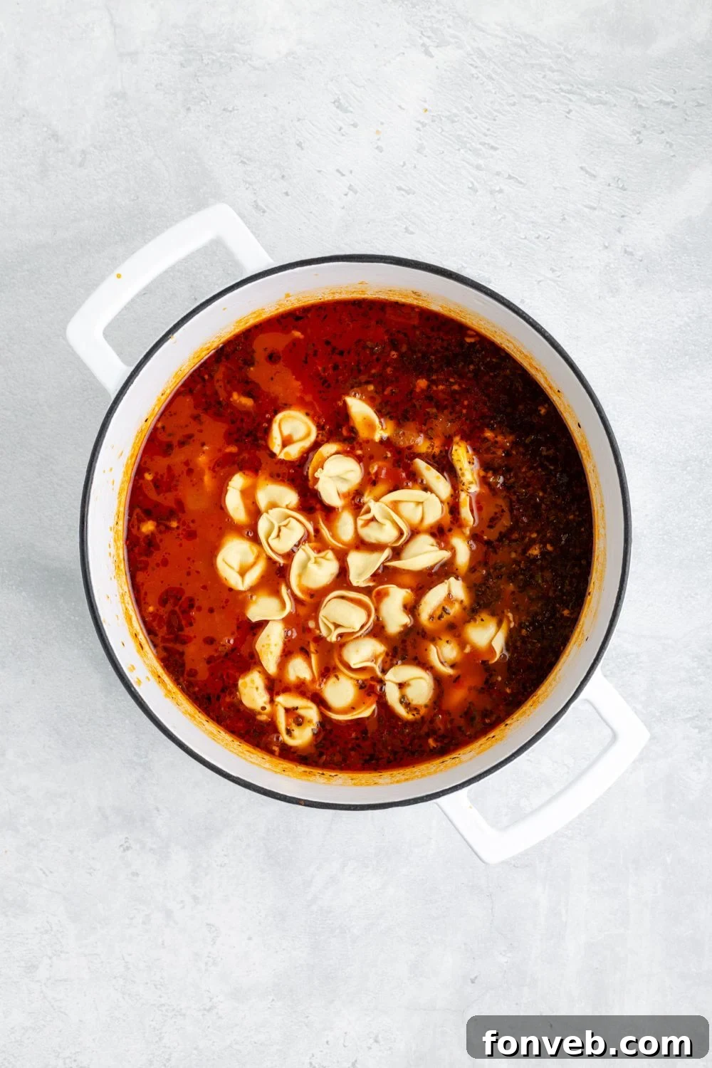 Fresh tortellini being carefully added into a white pot, mingling with the aromatic broth for Sausage Tortellini Soup