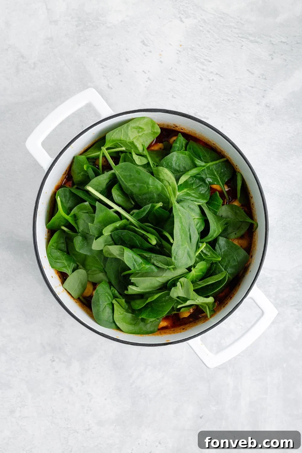 Fresh, vibrant spinach generously placed on top of a pot of simmering Sausage Tortellini Soup, ready to be stirred in