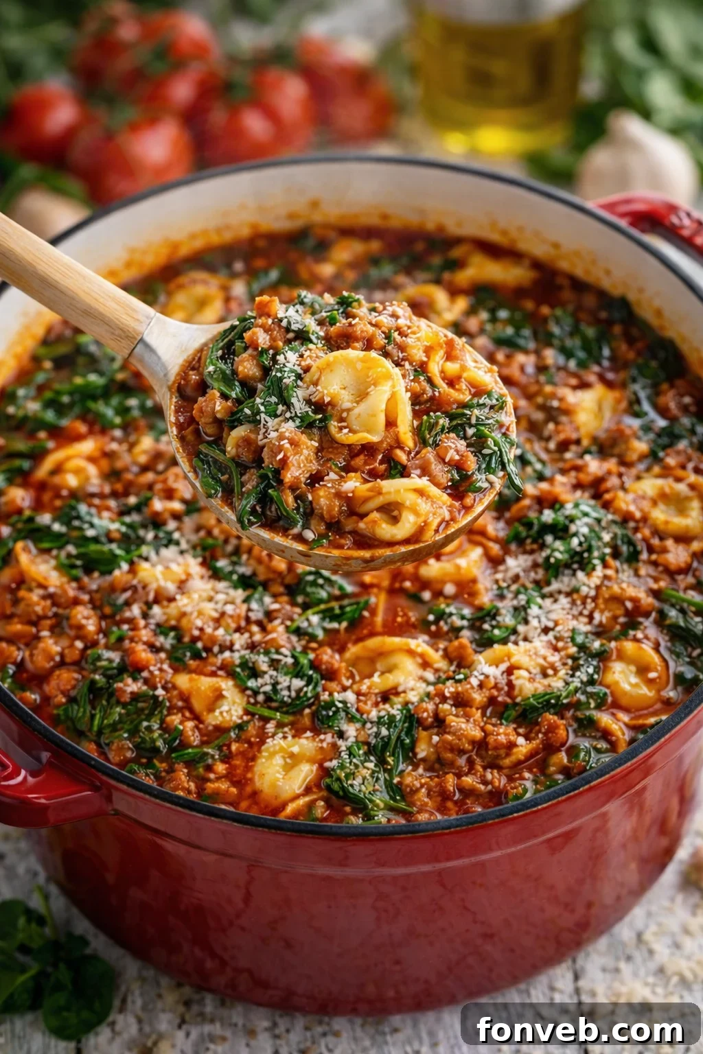 A generous spoonful of Sausage Spinach Tortellini Soup being lifted from a red Dutch oven, showcasing the delicious contents