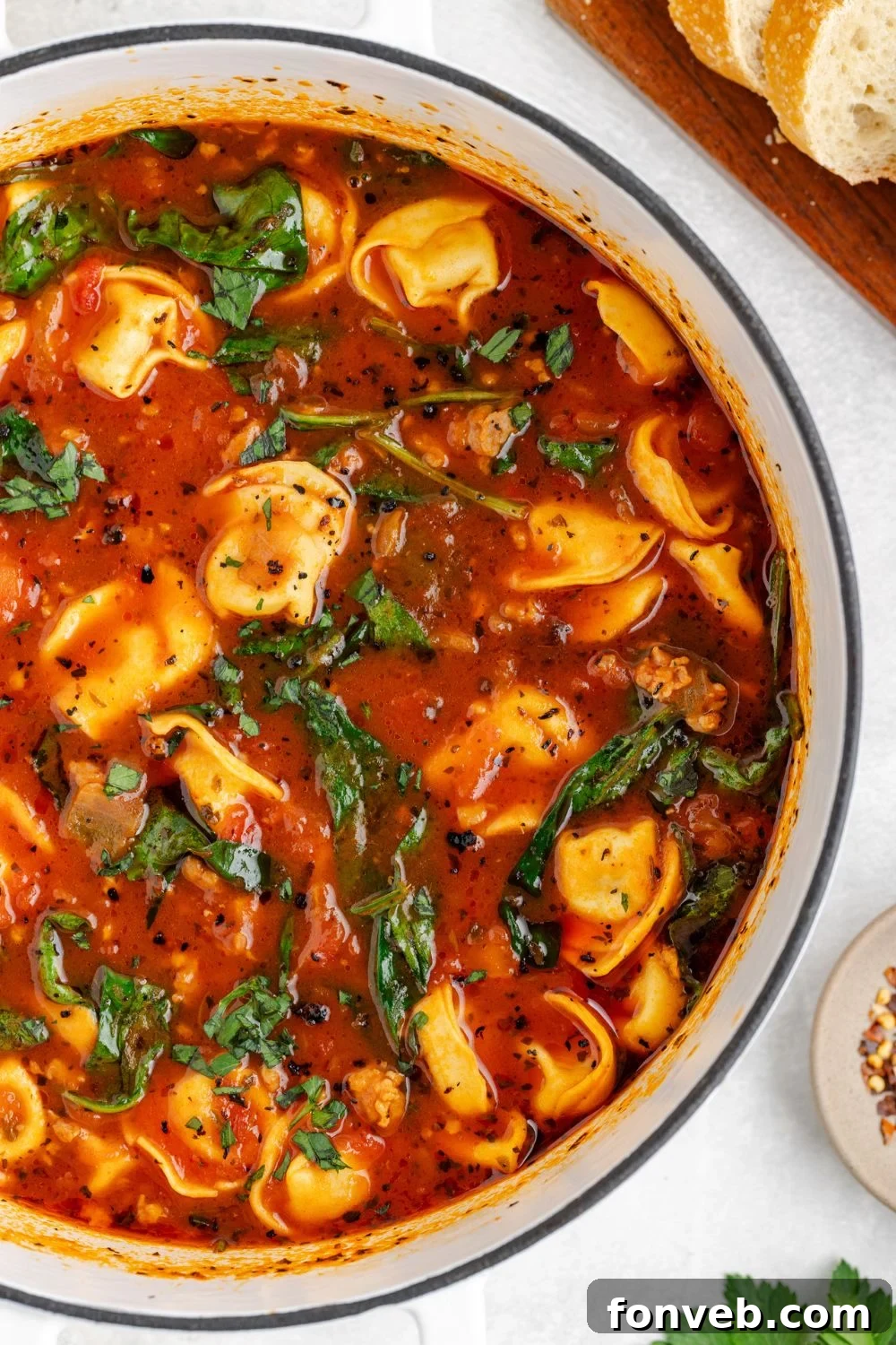 A top-down view of a generously sized stockpot filled with vibrant Sausage Tortellini Soup, accompanied by slices of French bread on a white table