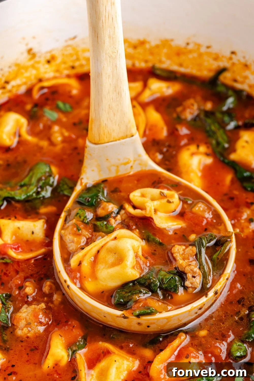 A ladle lifts a generous serving of Sausage Tortellini Soup, rich with pasta and sausage, directly from the pot