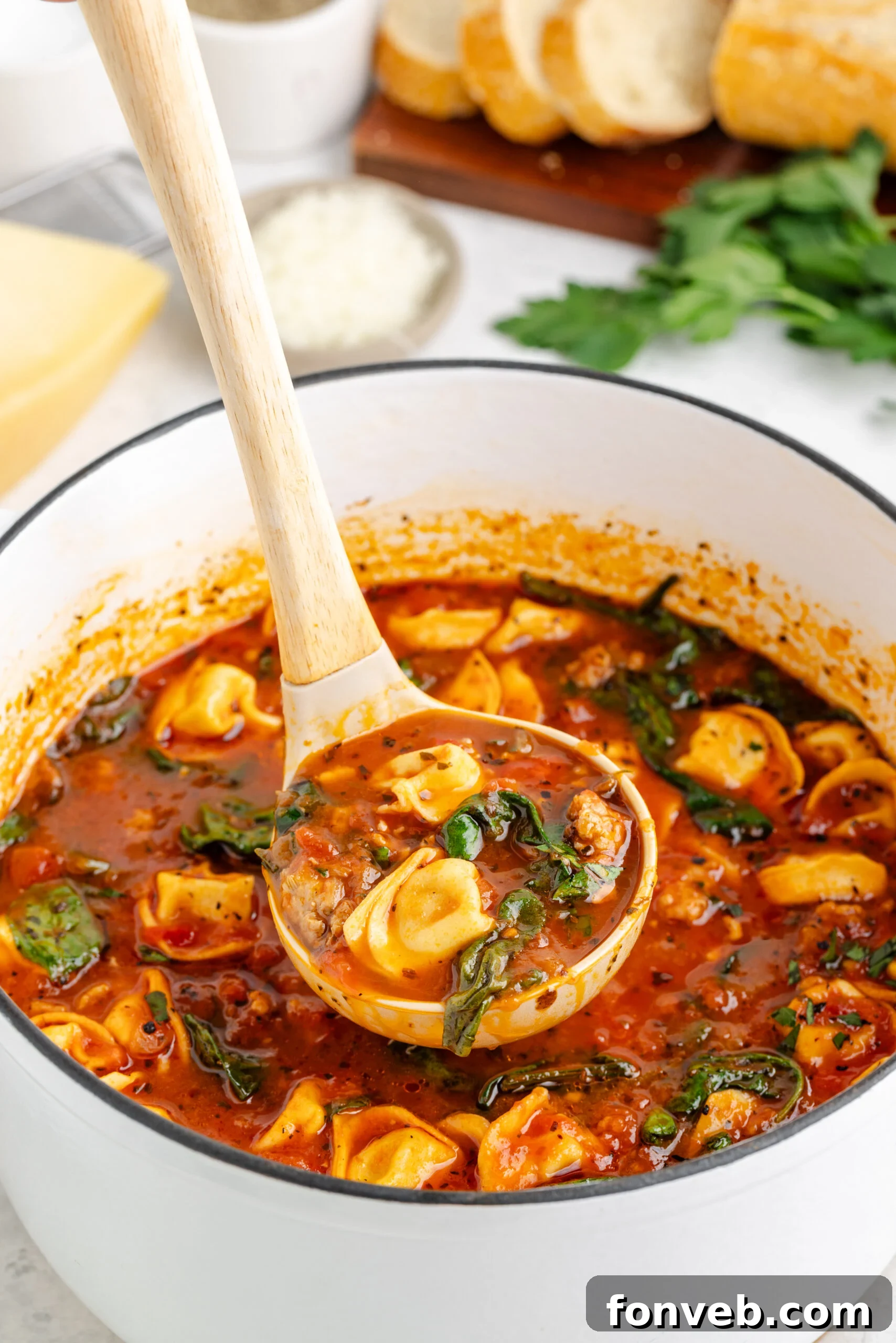 A large white pot overflowing with steaming Sausage Tortellini Soup, with a ladle poised to serve, promising comfort