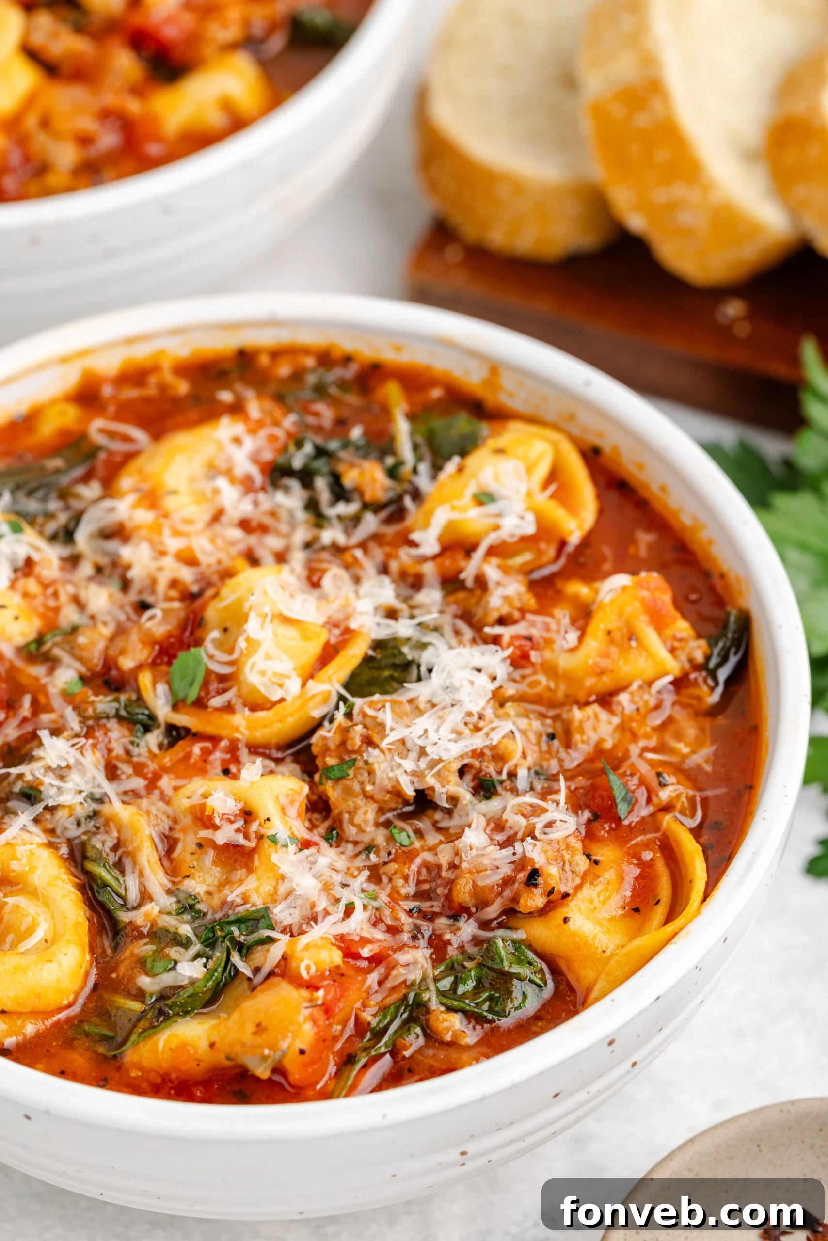 Close-up of Sausage Tortellini Soup served in a white bowl, garnished with freshly grated Parmesan cheese and a hint of fresh parsley