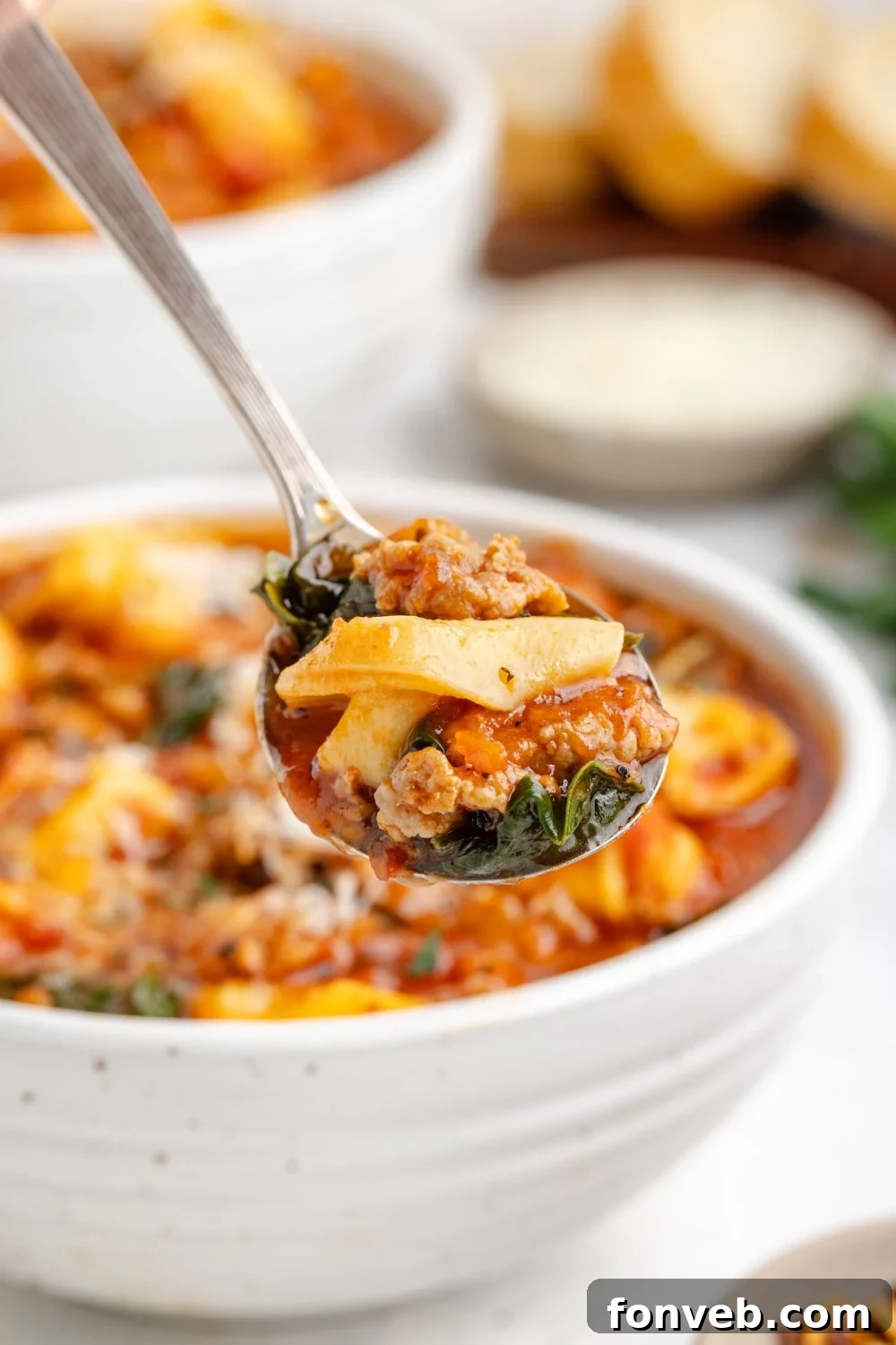 A pristine white bowl showcasing Sausage Tortellini Soup, with a spoon lifting a perfect portion above the bowl for a detailed view