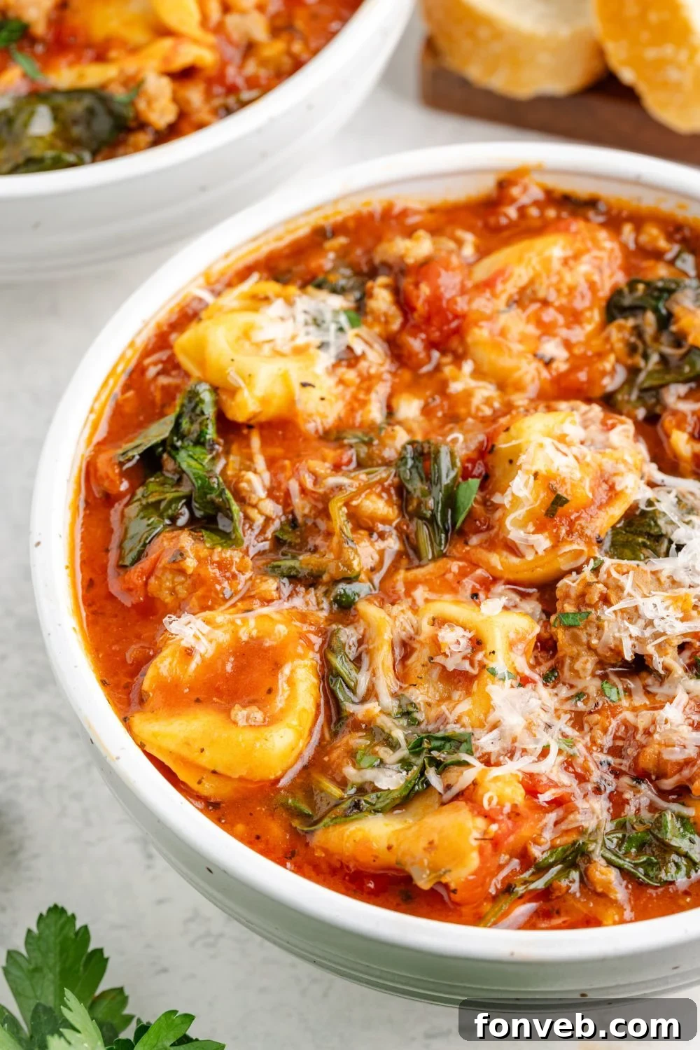 A side view of a pristine white bowl on a table, generously filled with Sausage Tortellini Soup and beautifully topped with freshly grated Parmesan cheese