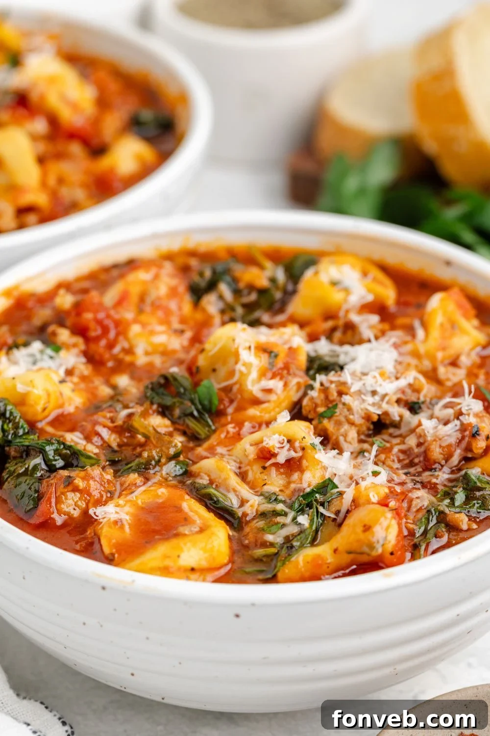 A side view of a white bowl filled with creamy Sausage Tortellini Soup, elegantly garnished with Parmesan cheese and a sprig of fresh parsley, resting on a table