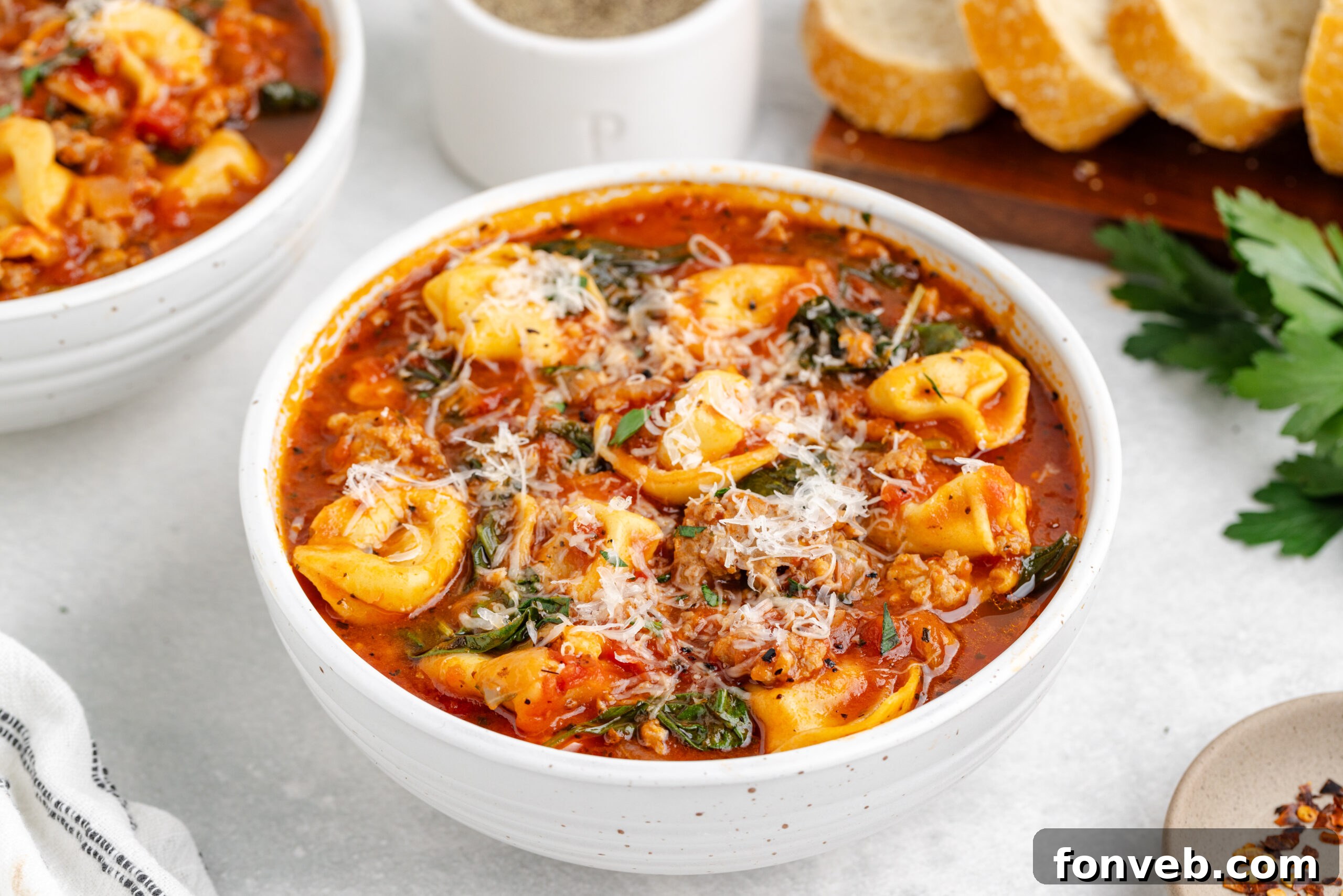 Sausage Tortellini Soup served in a white bowl, generously topped with freshly grated Parmesan cheese, resting on a beautiful white marble table