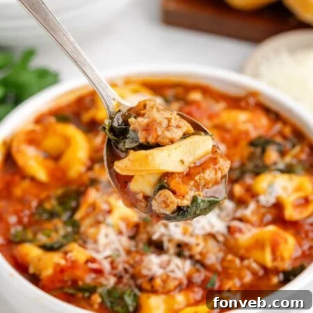 Sausage Tortellini Soup in a white bowl on table with a spoonful of soup just above the bowl