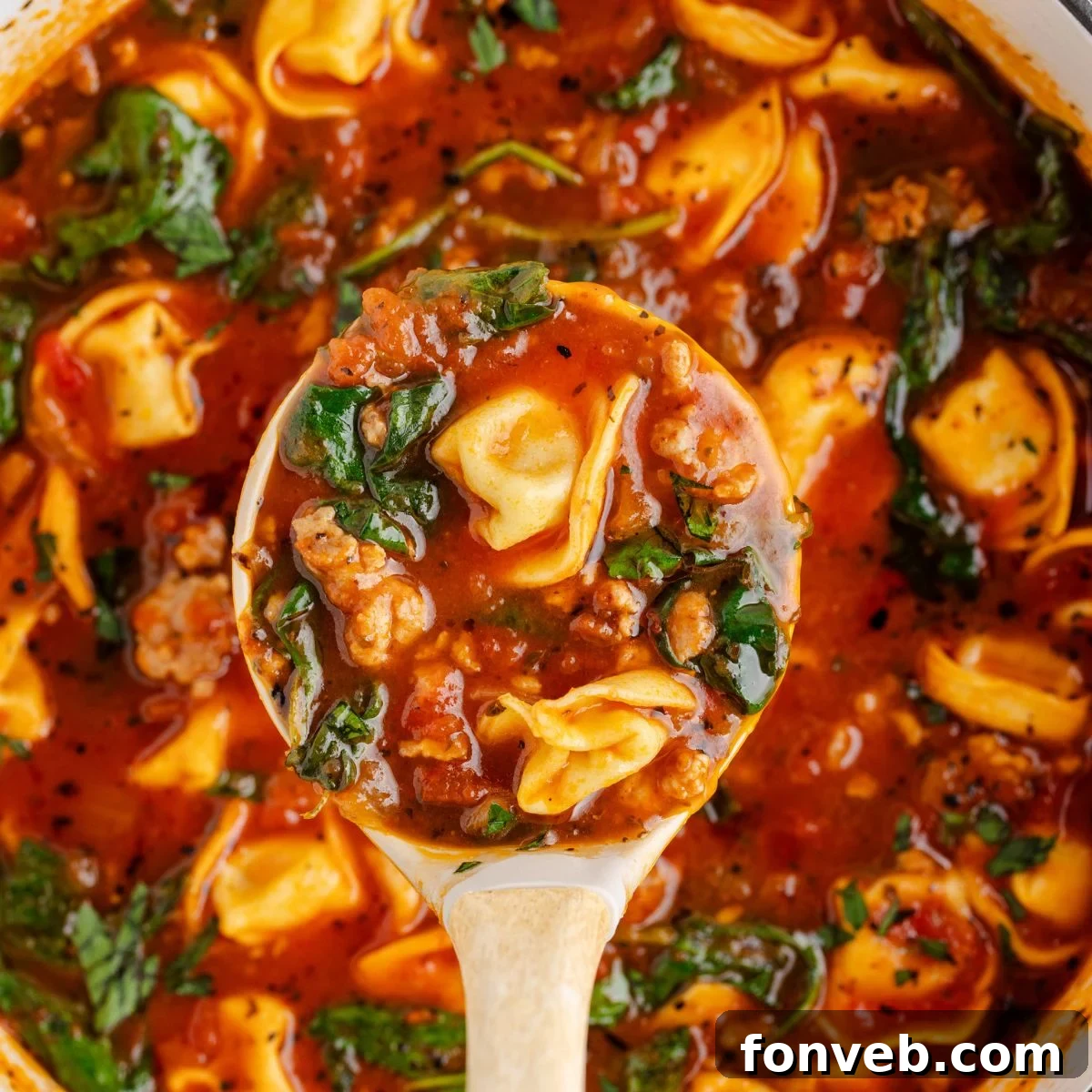 A ladle lifts a generous serving of One-Pot Sausage Tortellini Soup from a large pot, showcasing the rich broth and ingredients