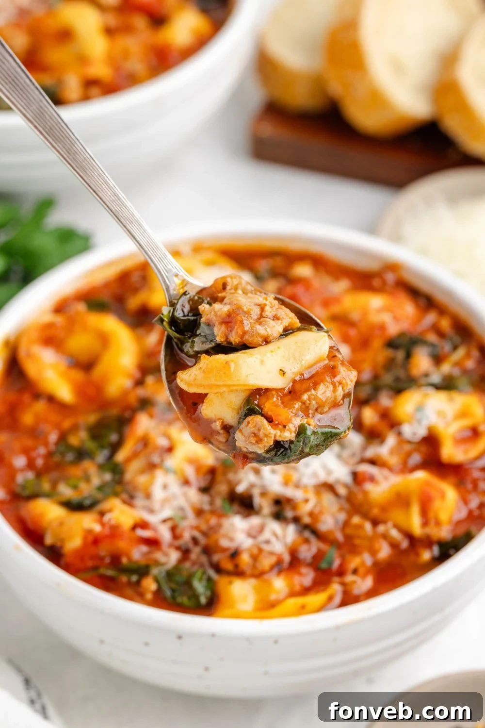 A white bowl filled with steaming Sausage Tortellini Soup, with a spoon hovering above, ready to enjoy