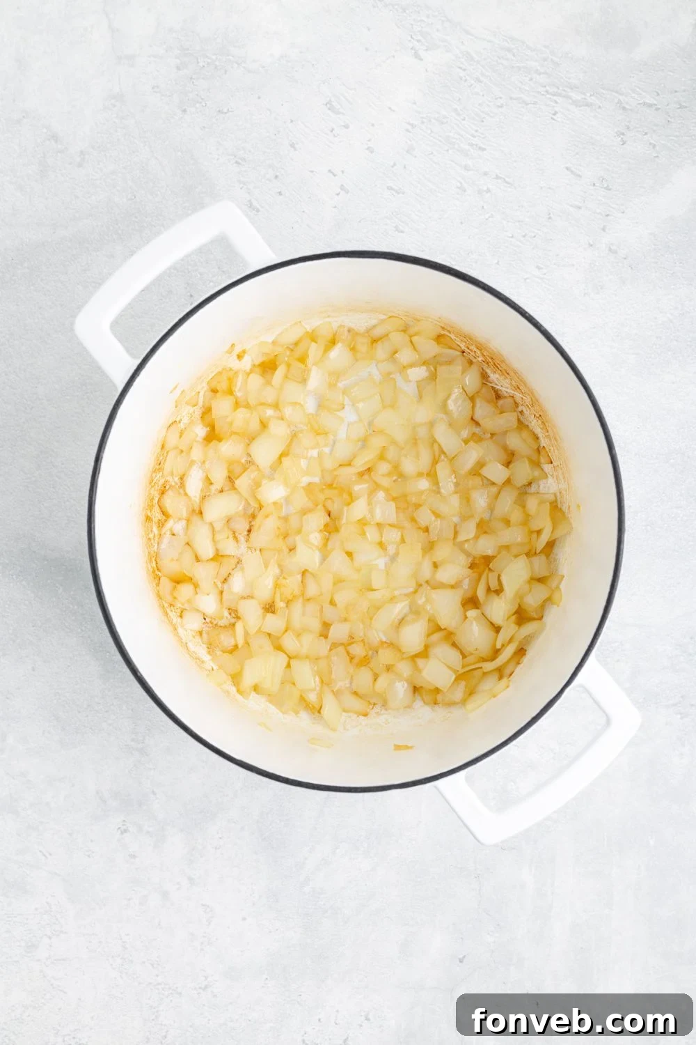 Translucent, sautéed onions glistening in a white pot on a clean white kitchen counter
