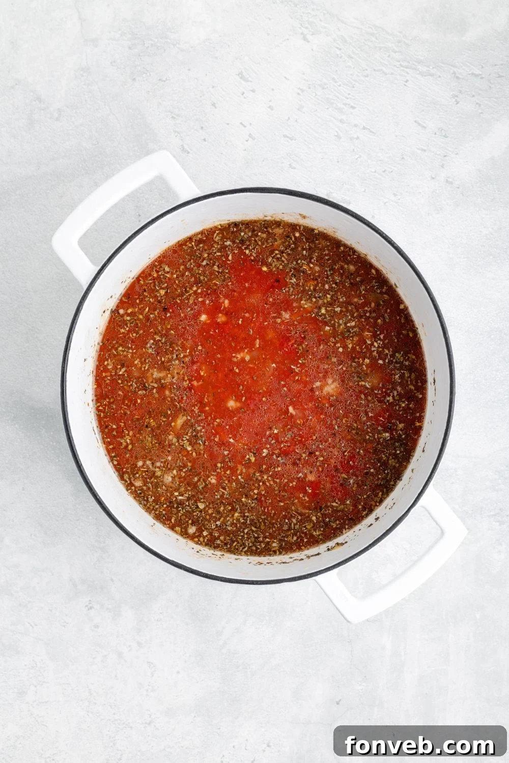 A vibrant tomato mixture, richly infused with fragrant spices, simmering gently in a white pot on a table, forming the base for Sausage Tortellini Soup