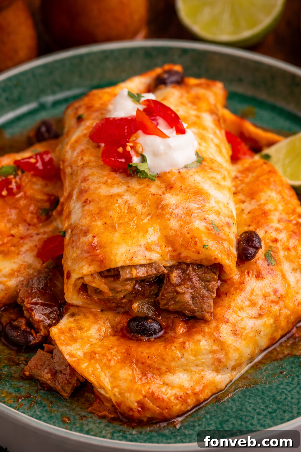 Steak Enchiladas on a green plate topped with sour cream and diced tomatoes 