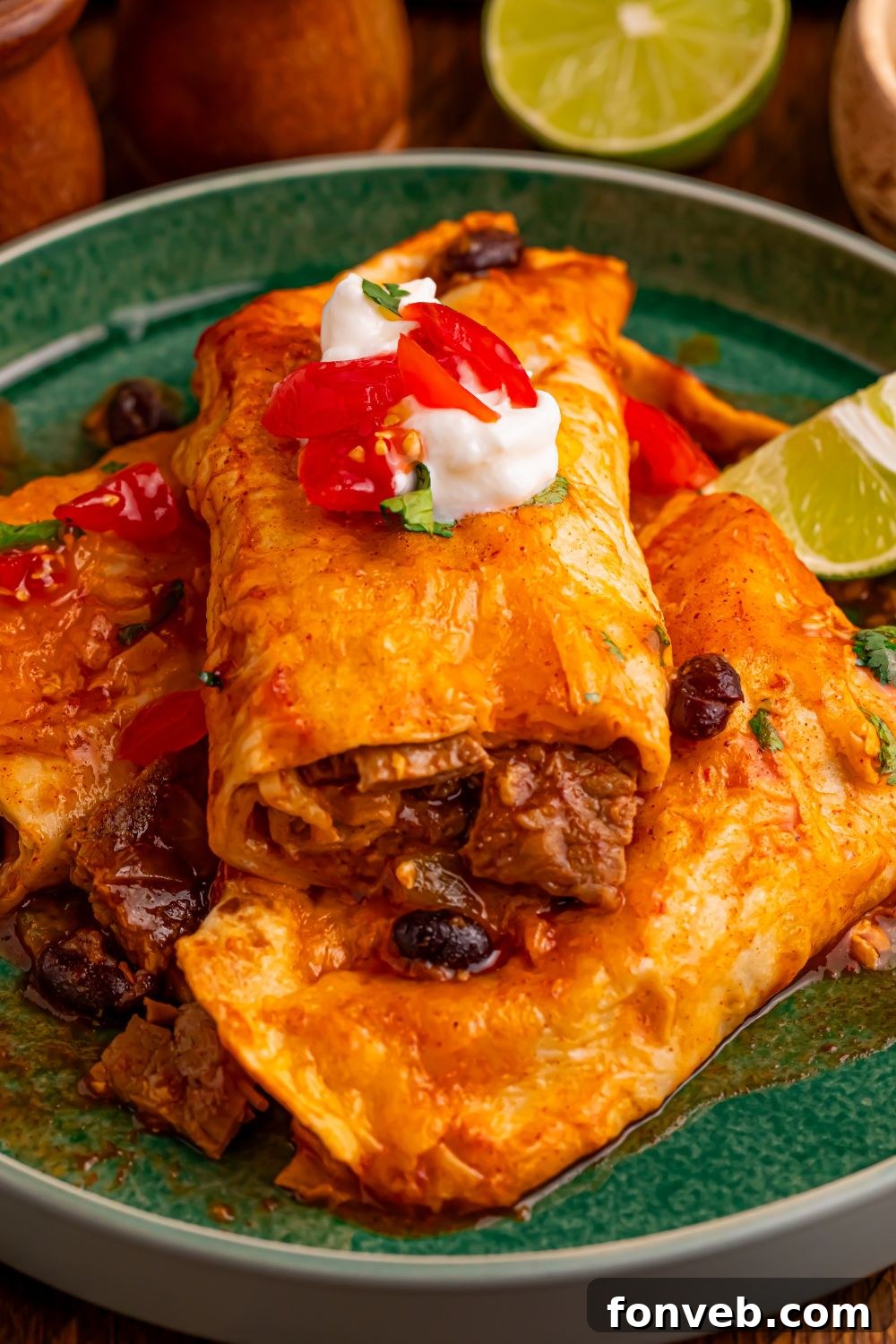 Steak Enchiladas on a plate with sour cream and salsa on top with a lime wedge to side on table 