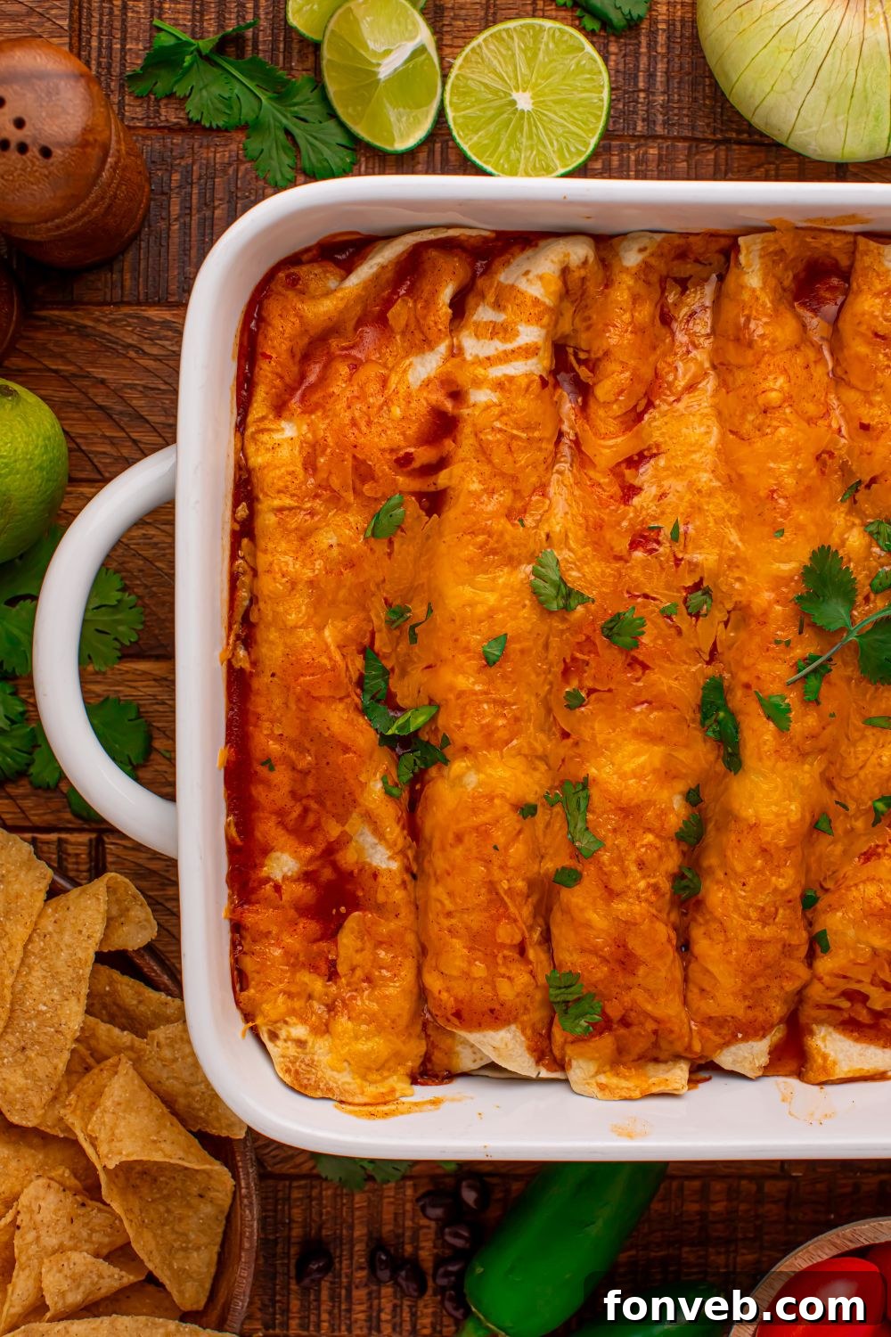 Steak Enchiladas in a white casserole dish with sliced limes on the wooden table and tortilla chips around the table 