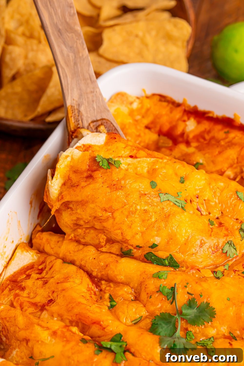 white enchilada pan with a wooden spatula scooping up one of the enchiladas from the pan with tortilla chips around the table 