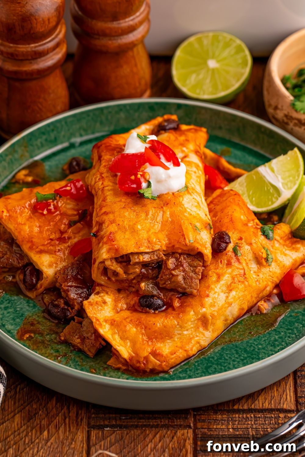 green plate with a few Steak Enchiladas on it and topped with sour cream, salsa, and lime wedge to side