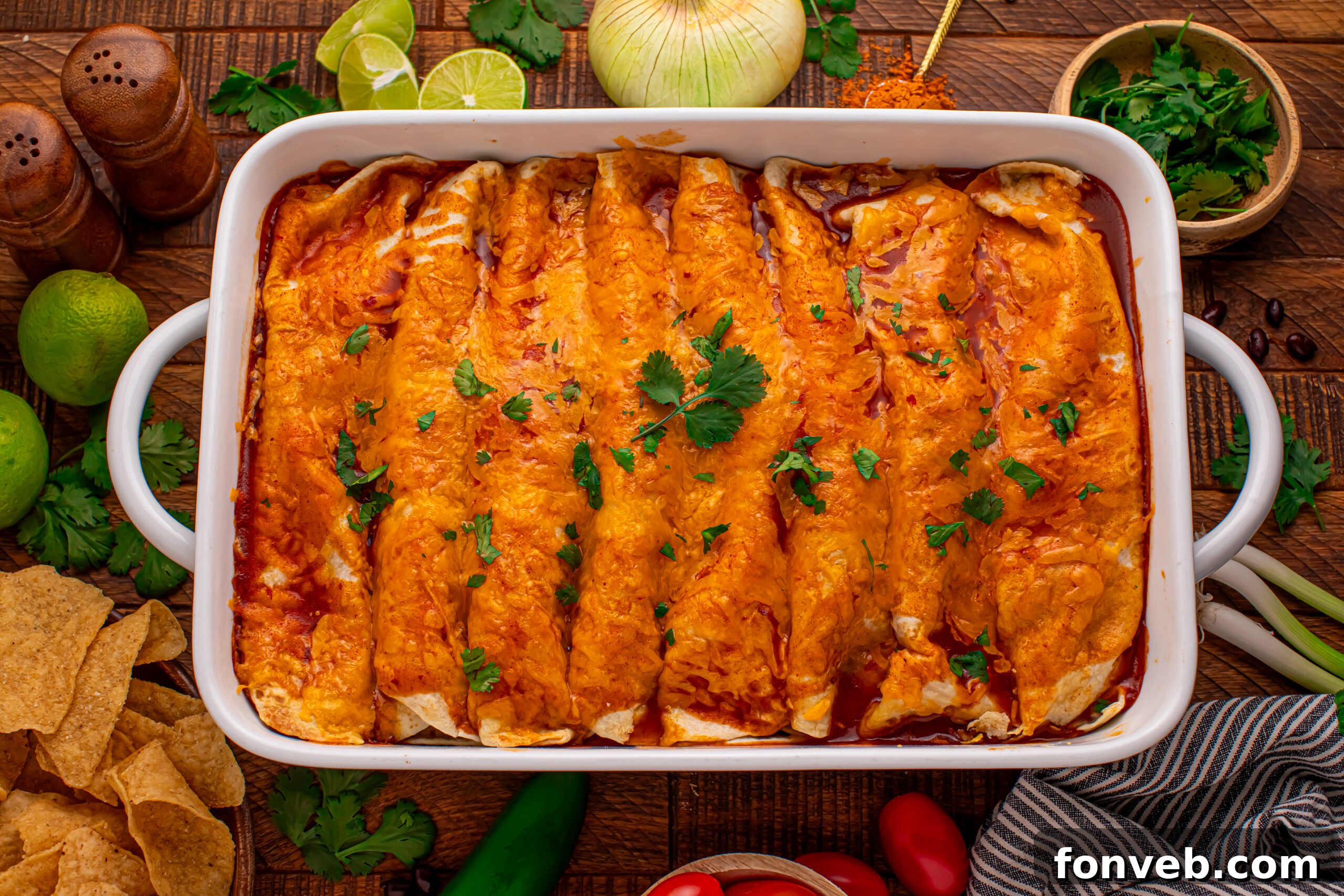 Steak Enchiladas in a white baking dish topped with sour cream and diced tomatoes 