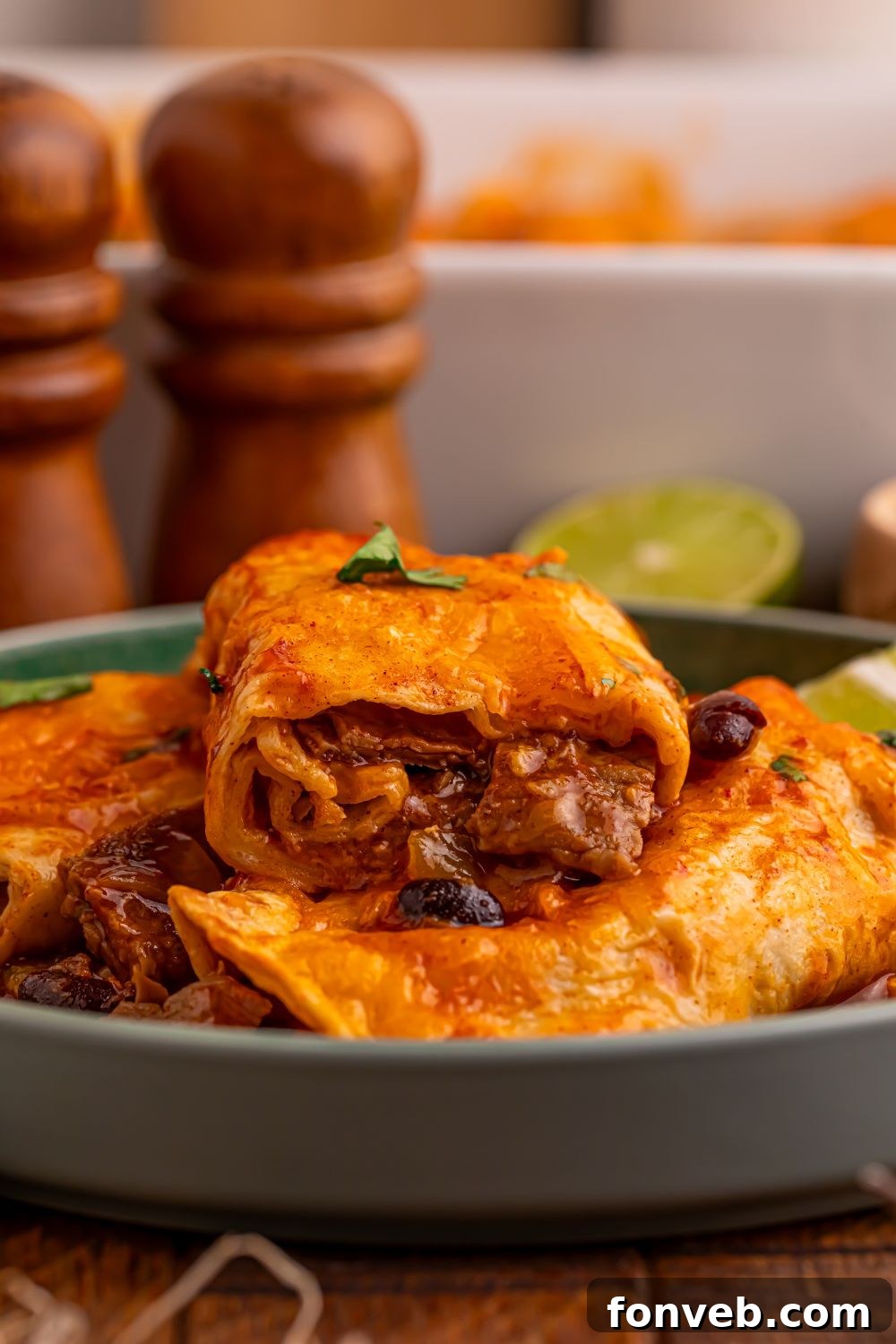 stack of Steak Enchiladas on a grey plate on table with some limes to the side and a white casserole dish behind it on the table 